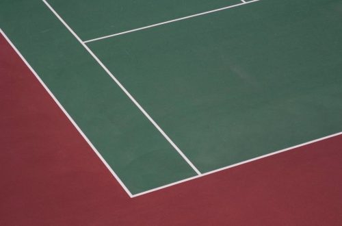 Угол теннисного корта с зелёным покрытием, белой разметкой и красной зоной вокруг